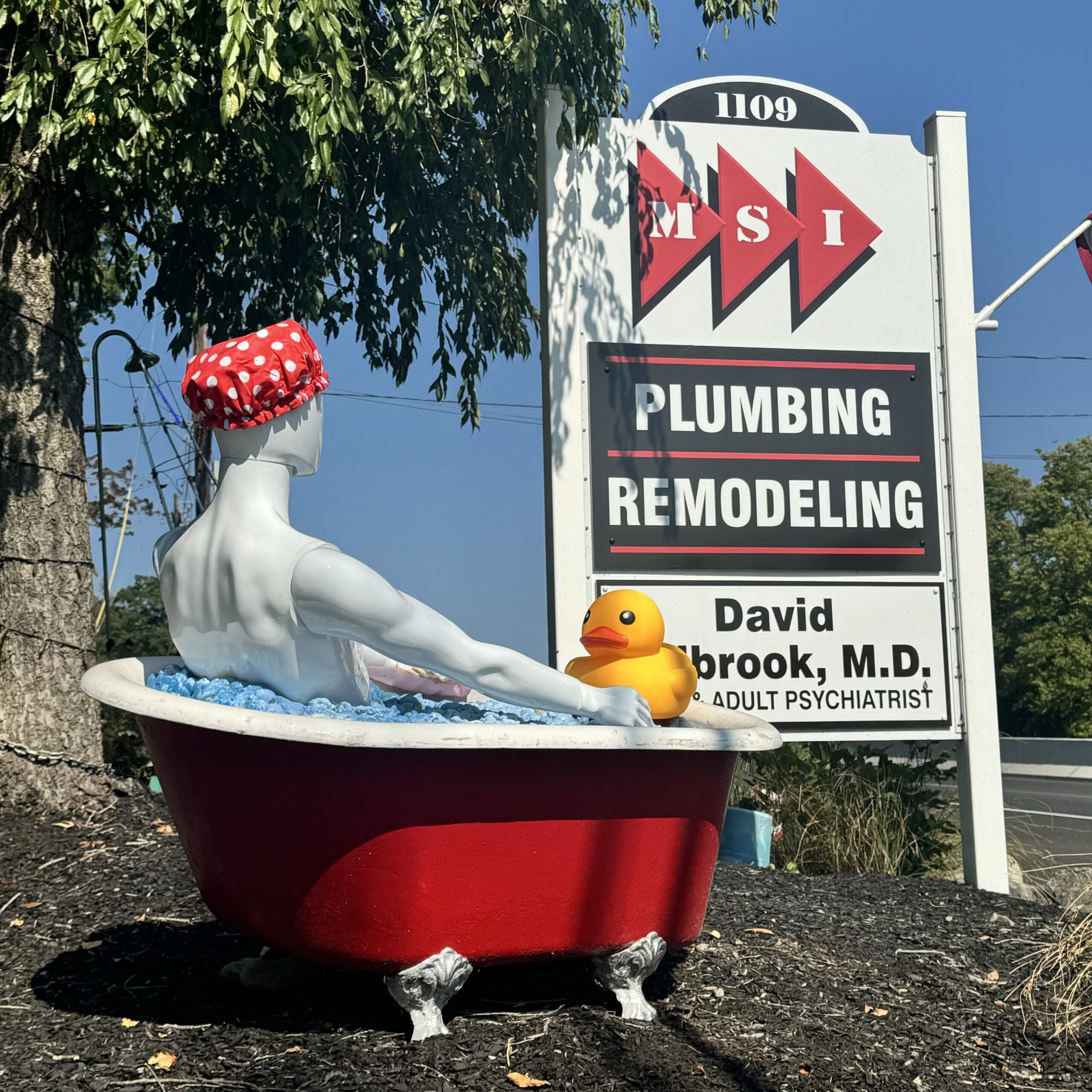 Mannequin taking a "bath" with a giant rubber duck in a red clawfoot tub next to the road sign for MSI Plumbing and Remodeling